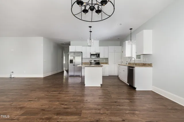 a view of kitchen with stainless steel appliances granite countertop a wooden floor a stove a sink and white cabinets