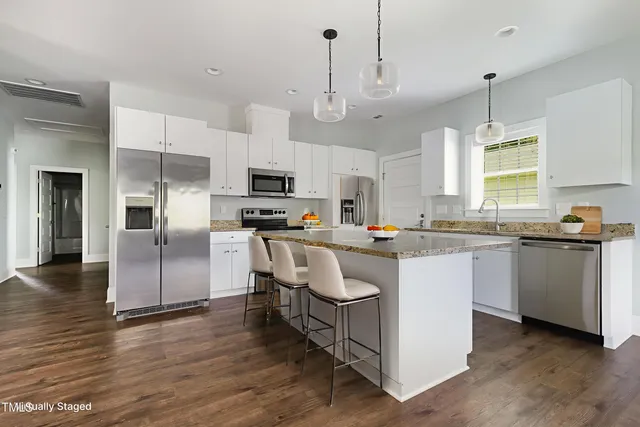 a kitchen with kitchen island granite countertop a refrigerator a sink dishwasher a stove and white cabinets with wooden floor