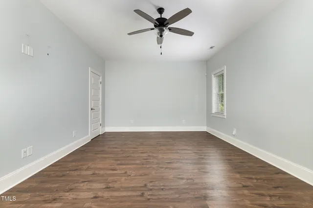an empty room with wooden floor ceiling fan and windows