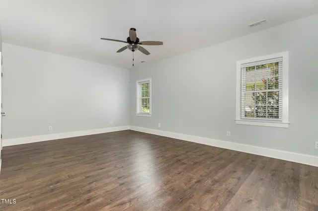 an empty room with wooden floor ceiling fan and windows