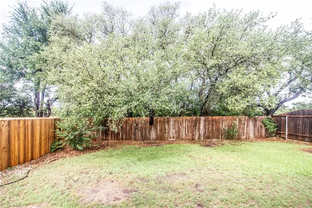 a view of a backyard with large tree and wooden fence