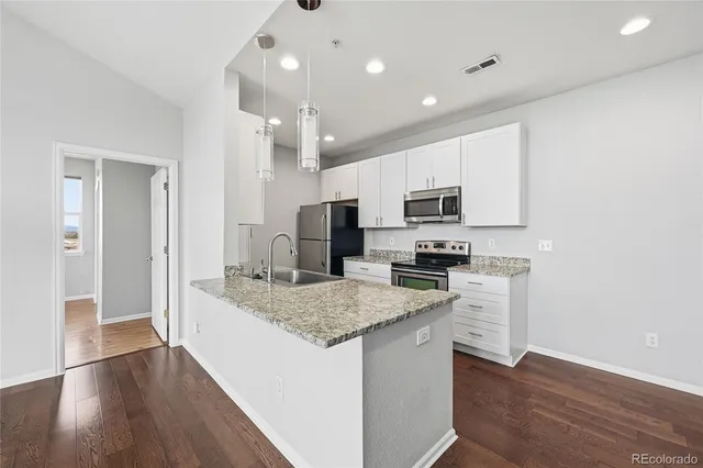 a kitchen with kitchen island granite countertop stainless steel appliances cabinets a sink and a wooden floor