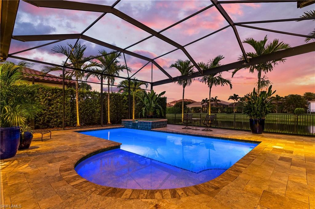 Pool at dusk featuring a pool with connected hot tub, a sunroom, glass enclosure, and a patio