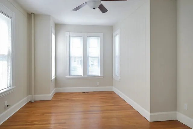 an empty room with wooden floor fan and windows
