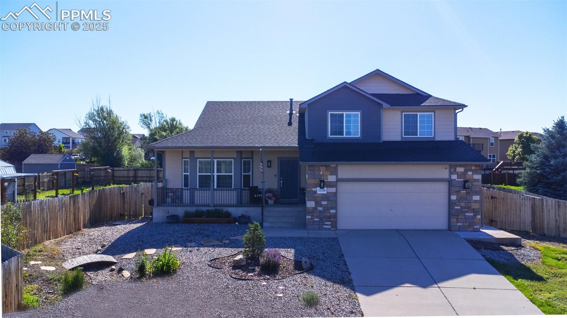11310 Falling Star Road Fountain, CO 80817 - Photo 1 of 34 View of front of property featuring a porch, concrete driveway, an attached garage, stone siding, and roof with shingles