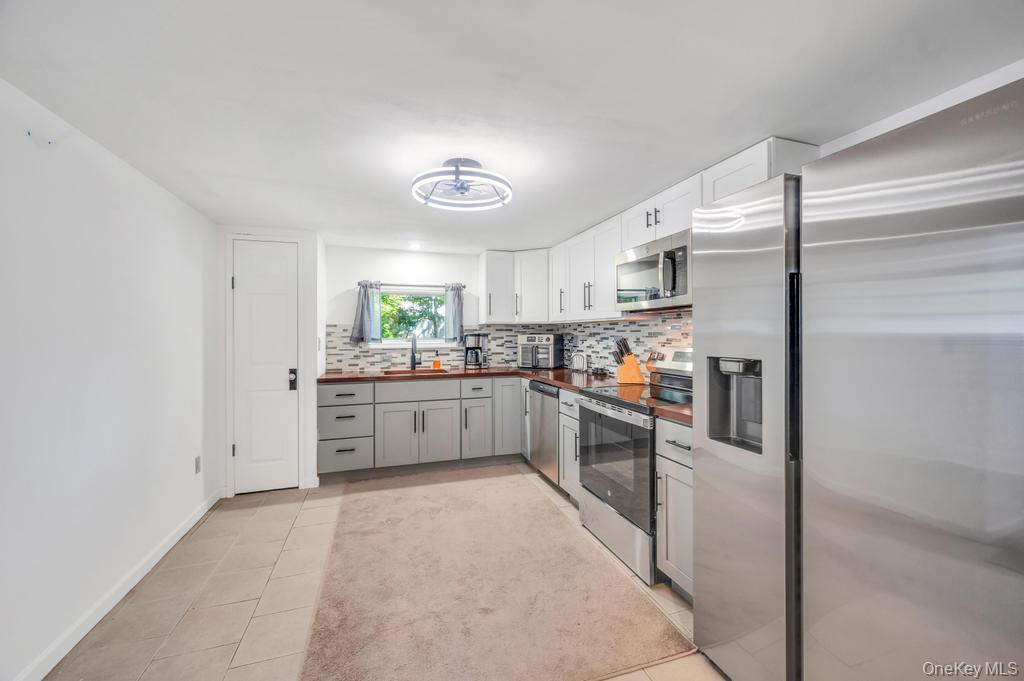 5 Panther Path Miller Place, NY 11764 - Photo 14 of 37 Kitchen featuring appliances with stainless steel finishes, decorative backsplash, light tile patterned flooring, white cabinets, and butcher block counters