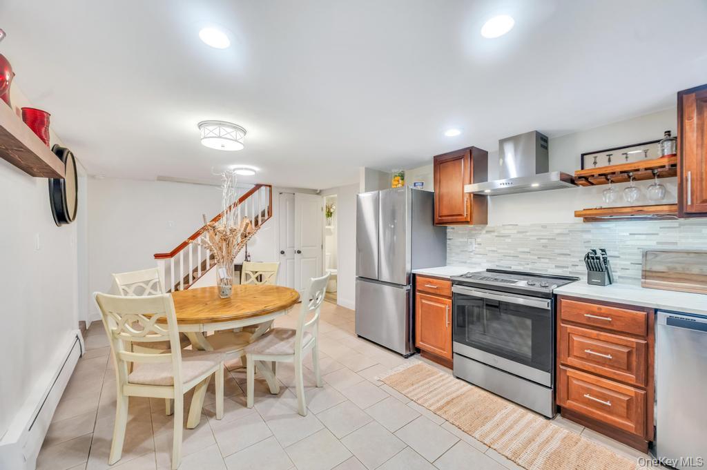 5 Panther Path Miller Place, NY 11764 - Photo 24 of 37 Kitchen with a baseboard heating unit, stainless steel appliances, open shelves, wall chimney exhaust hood, and backsplash
