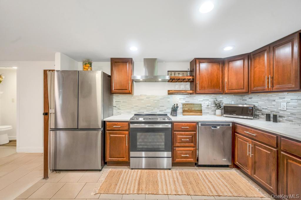 5 Panther Path Miller Place, NY 11764 - Photo 25 of 37 Kitchen with stainless steel appliances, wall chimney range hood, light tile patterned floors, open shelves, and backsplash