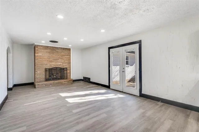 an empty room with wooden floor fireplace and windows