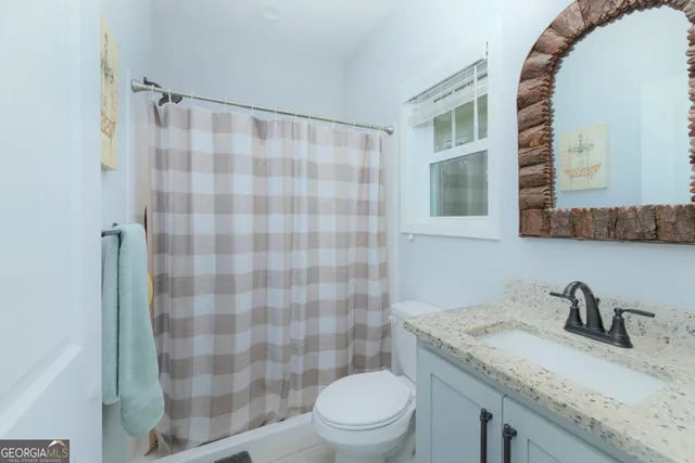 a bathroom with a granite countertop sink a toilet a mirror and shower curtain