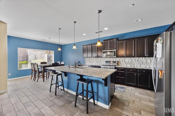 a kitchen with stainless steel appliances granite countertop a stove top oven a refrigerator a sink and a dining table with wooden floor