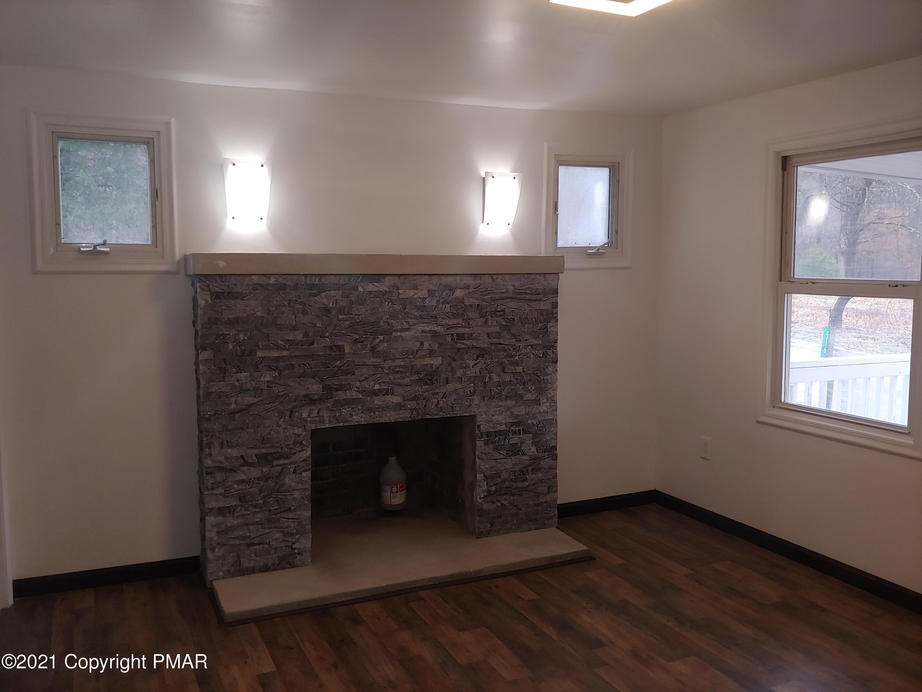516 Red Rock Road Cresco, PA 18326 - Photo 8 of 47 an empty room with wooden floor a fireplace and windows