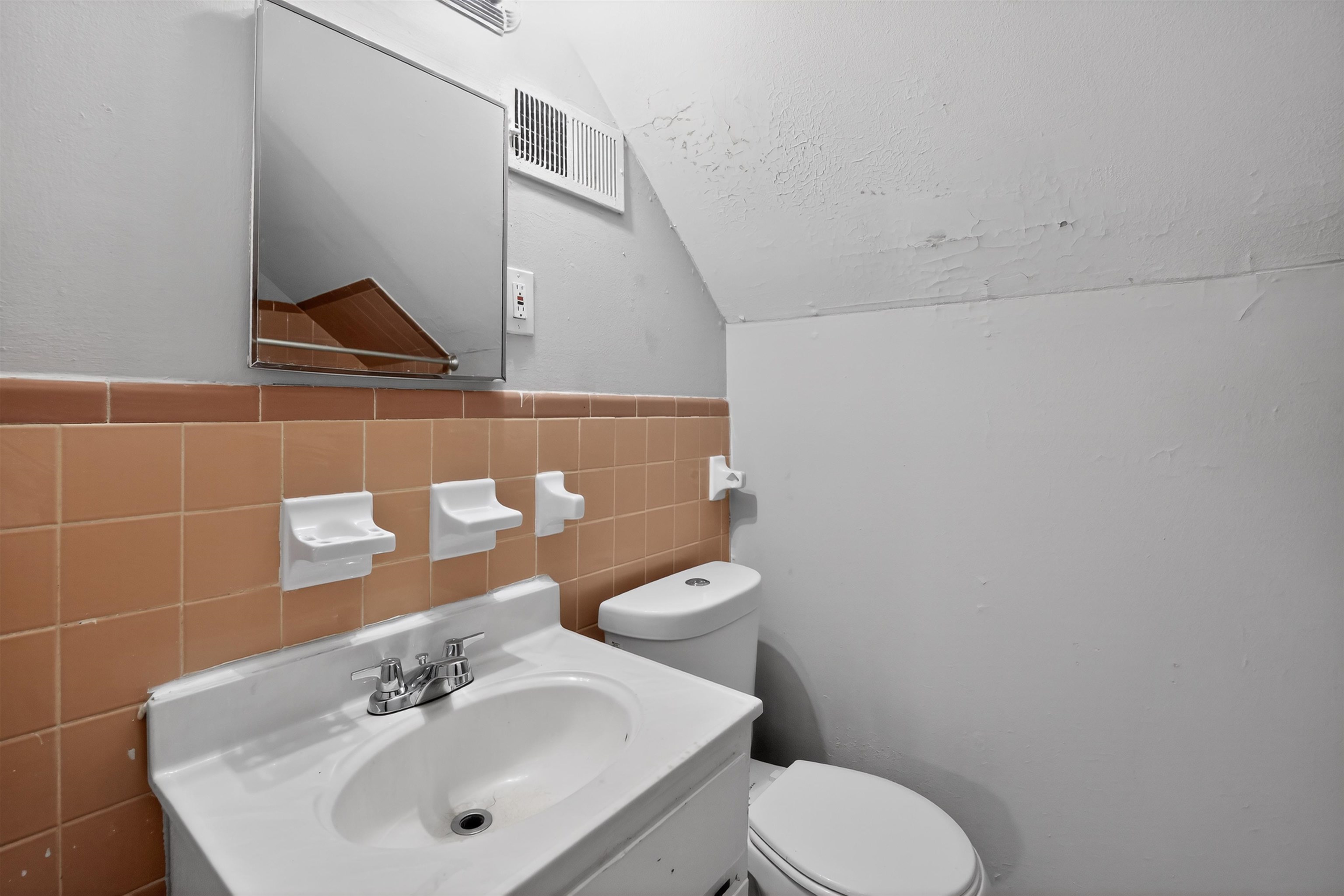5124 Gill Road Memphis, TN 38109 - Photo 22 of 33 Bathroom featuring a wall-mounted mirror, vanity with an integrated sink, dual-handle faucet, ceramic tile wainscoting, and a white toilet