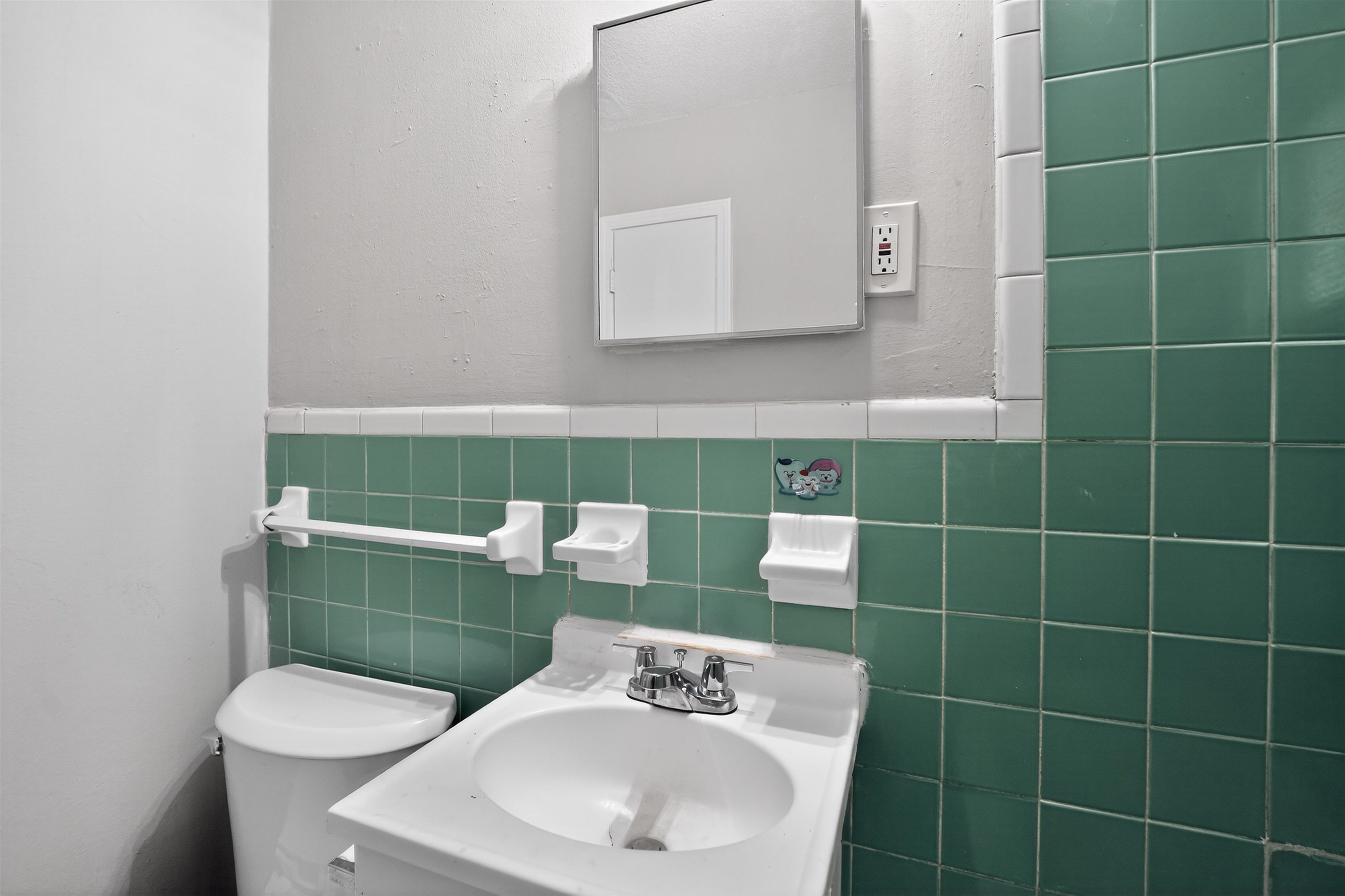 5124 Gill Road Memphis, TN 38109 - Photo 24 of 33 Bathroom featuring green subway tile wainscoting, a wall-mounted sink with chrome fixtures, a medicine cabinet, and a white toilet