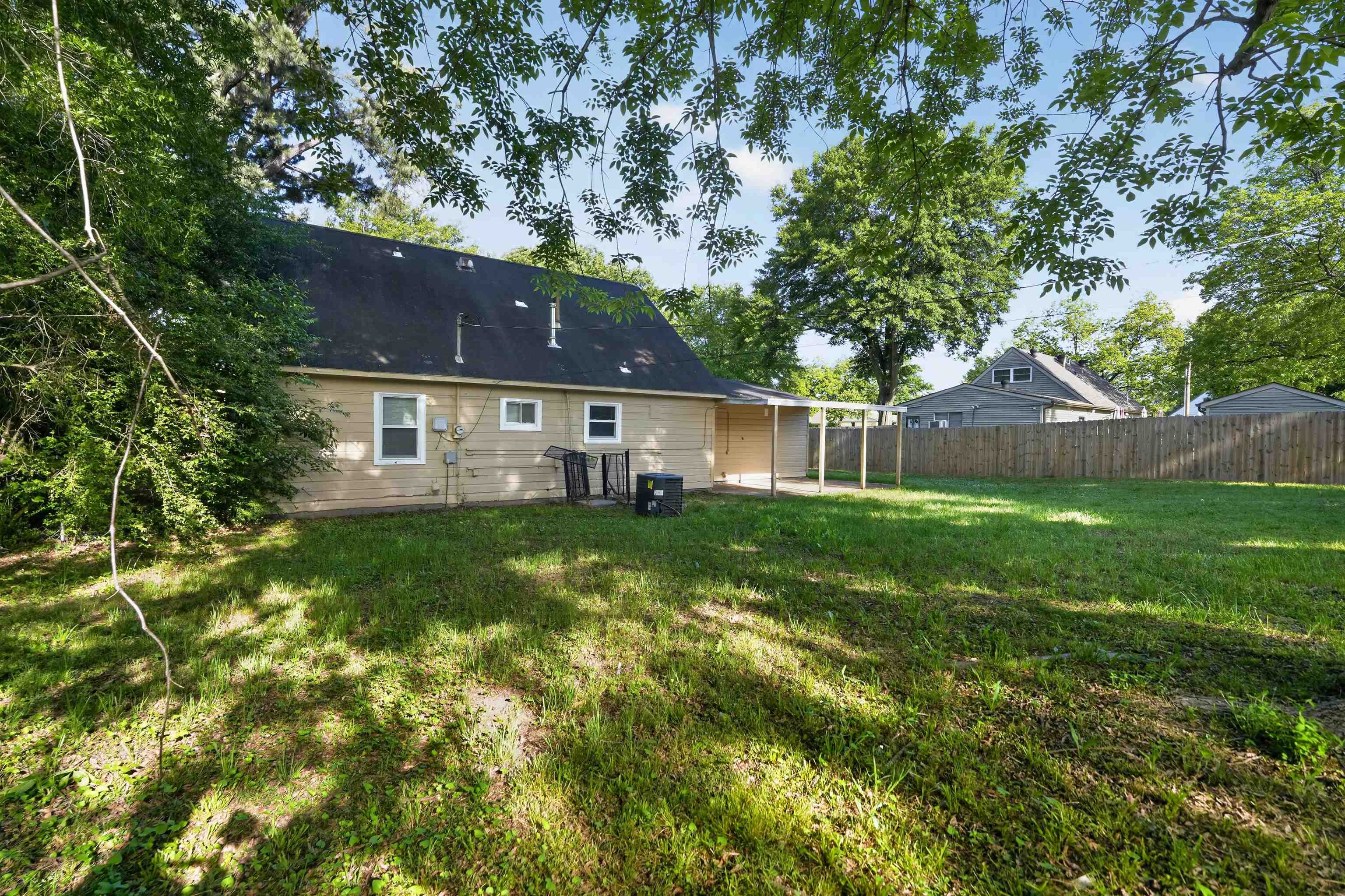 5124 Gill Road Memphis, TN 38109 - Photo 7 of 33 Expansive rear yard featuring green lawn, mature trees, wood privacy fencing, and a covered patio area