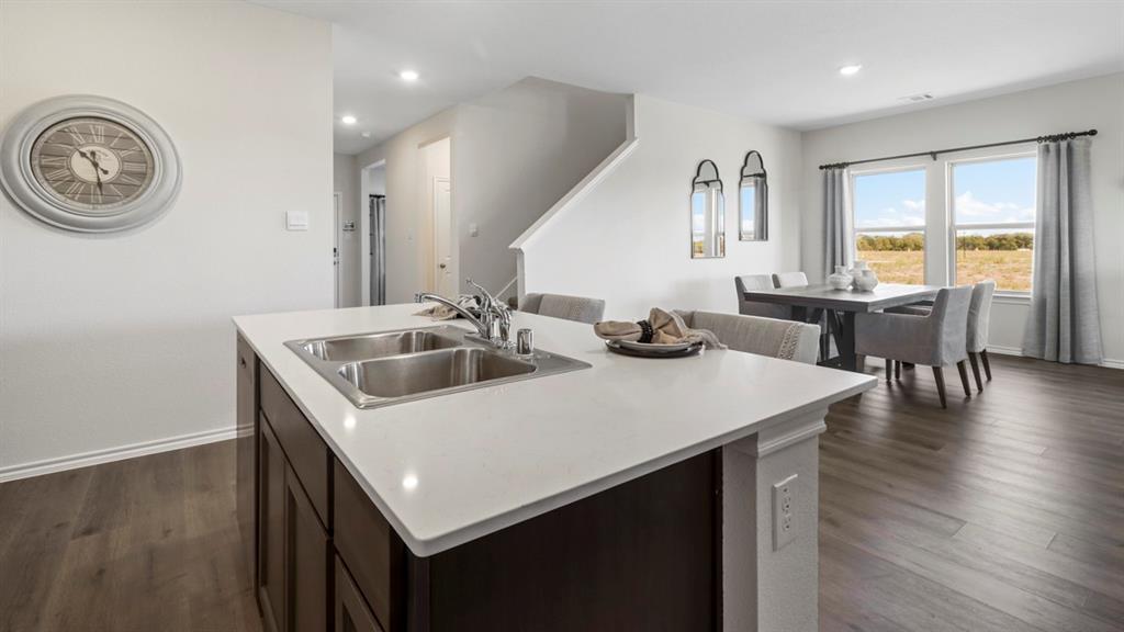 636 Dunham Road Nevada, TX 75173 - Photo 21 of 31 Kitchen island featuring a stainless steel double basin sink with chrome faucet, white countertop, and dark wood-finish cabinetry