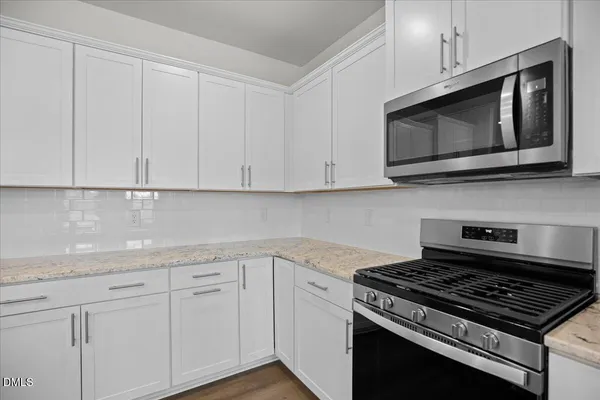 a large kitchen with stainless steel appliances granite countertop a sink a stove a refrigerator and white cabinets with wooden floor