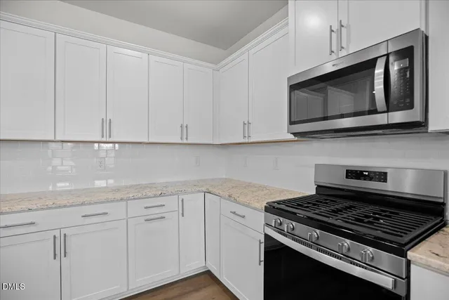 a large kitchen with stainless steel appliances granite countertop a sink a stove a refrigerator and white cabinets with wooden floor