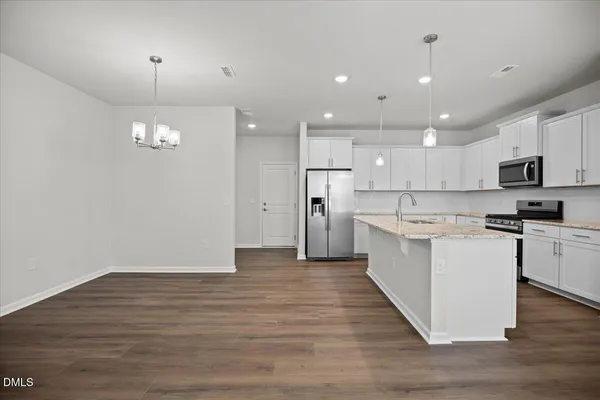 a kitchen with kitchen island granite countertop a stove top oven a sink dishwasher a refrigerator and white cabinets with wooden floor
