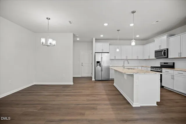 a kitchen with kitchen island granite countertop a stove top oven a sink dishwasher a refrigerator and white cabinets with wooden floor