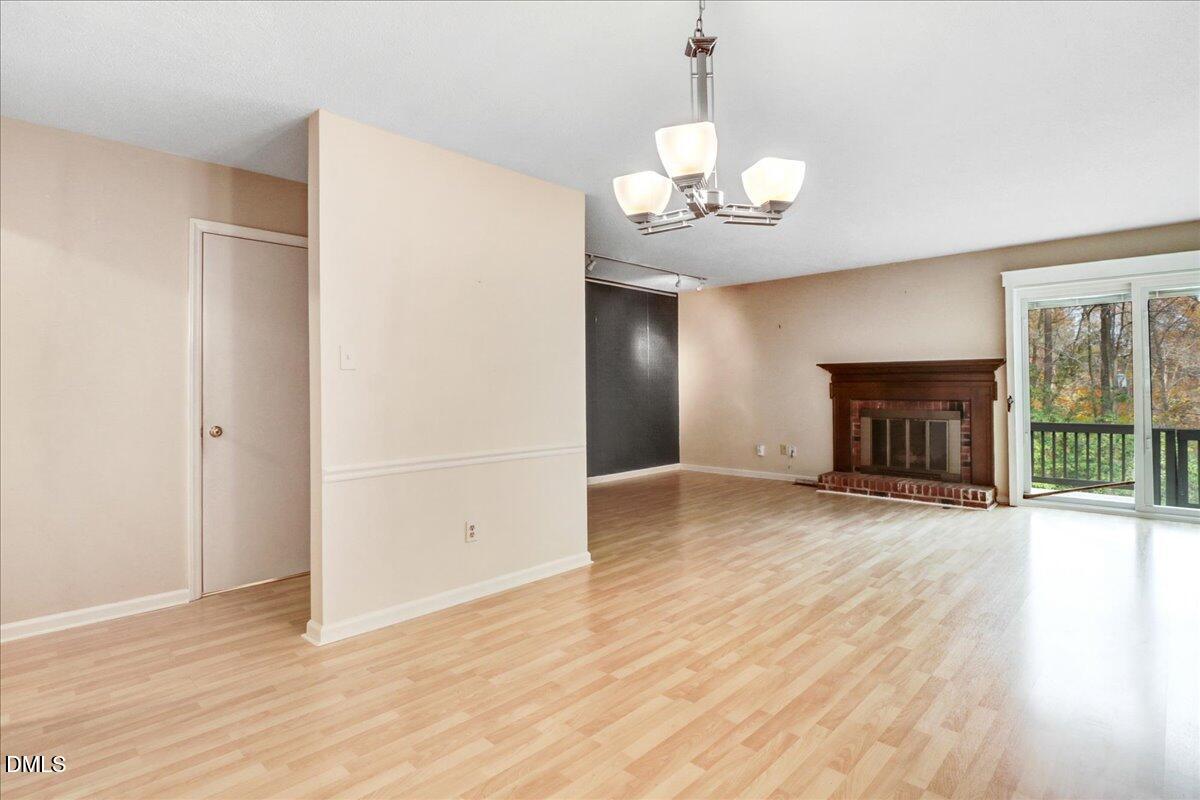 5738 3 Oaks Drive Raleigh, NC 27612 - Photo 12 of 32 an empty room with wooden floor fireplace and chandelier