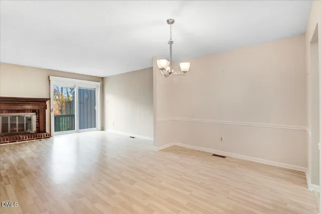 an empty room with wooden floor fireplace and chandelier