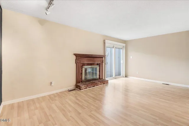 a view of an empty room with wooden floor and a fireplace