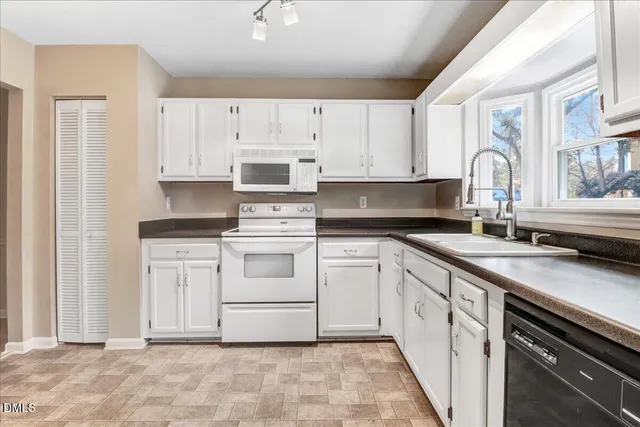 a kitchen with white cabinets appliances a sink and a window