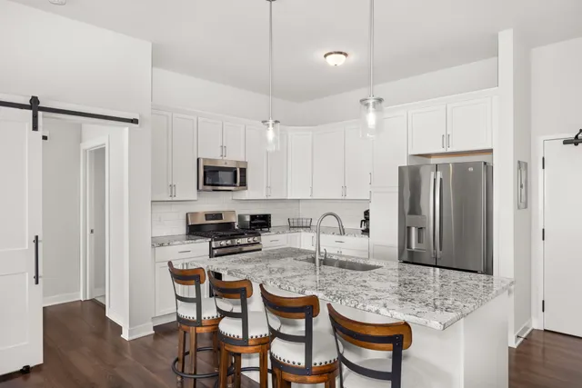 a kitchen with stainless steel appliances granite countertop a dining table chairs refrigerator and sink
