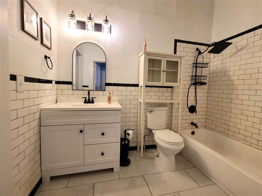 615 West Gandy Street Denison, TX 75020 - Photo 17 of 20 Bathroom featuring vanity, tile walls, tub / shower combination, wainscoting, and a textured wall