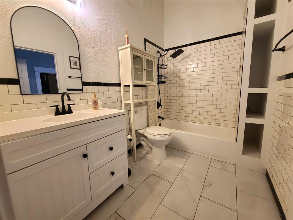 615 West Gandy Street Denison, TX 75020 - Photo 18 of 20 Full bathroom with vanity, washtub / shower combination, marble look tiles, tile walls, and a textured wall