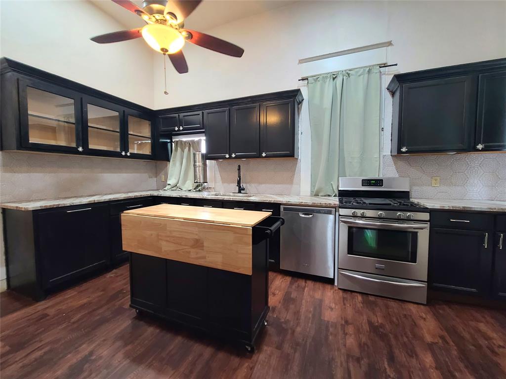 615 West Gandy Street Denison, TX 75020 - Photo 10 of 20 Kitchen featuring appliances with stainless steel finishes, dark cabinets, glass insert cabinets, decorative backsplash, and a towering ceiling
