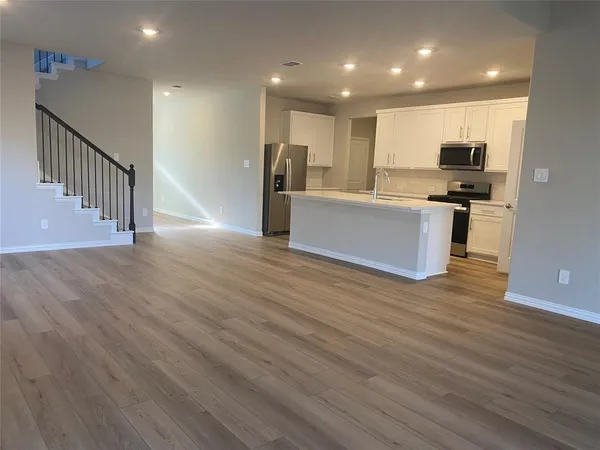 a view of kitchen with kitchen island granite countertop a stove top oven a sink and a potted plant on wooden floor