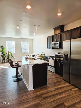 a kitchen with kitchen island a counter top space a sink a refrigerator and a view of living room