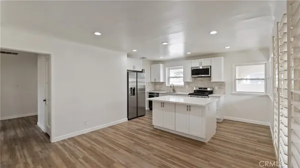 a kitchen with stainless steel appliances granite countertop a refrigerator a sink dishwasher a stove top oven a refrigerator and white cabinets with wooden floor