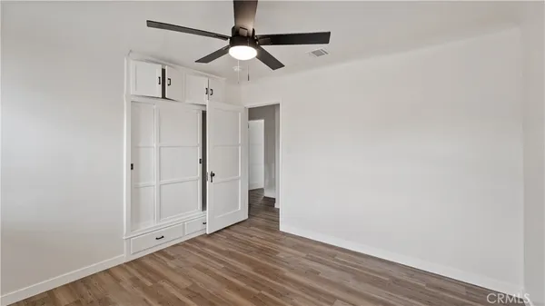 an empty room with wooden floor ceiling fan and windows