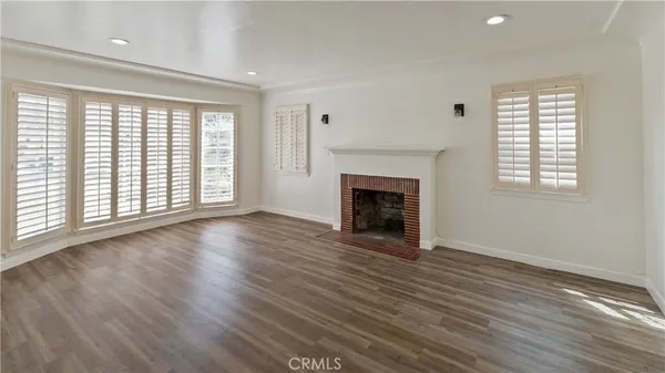 an empty room with wooden floor fireplace and windows