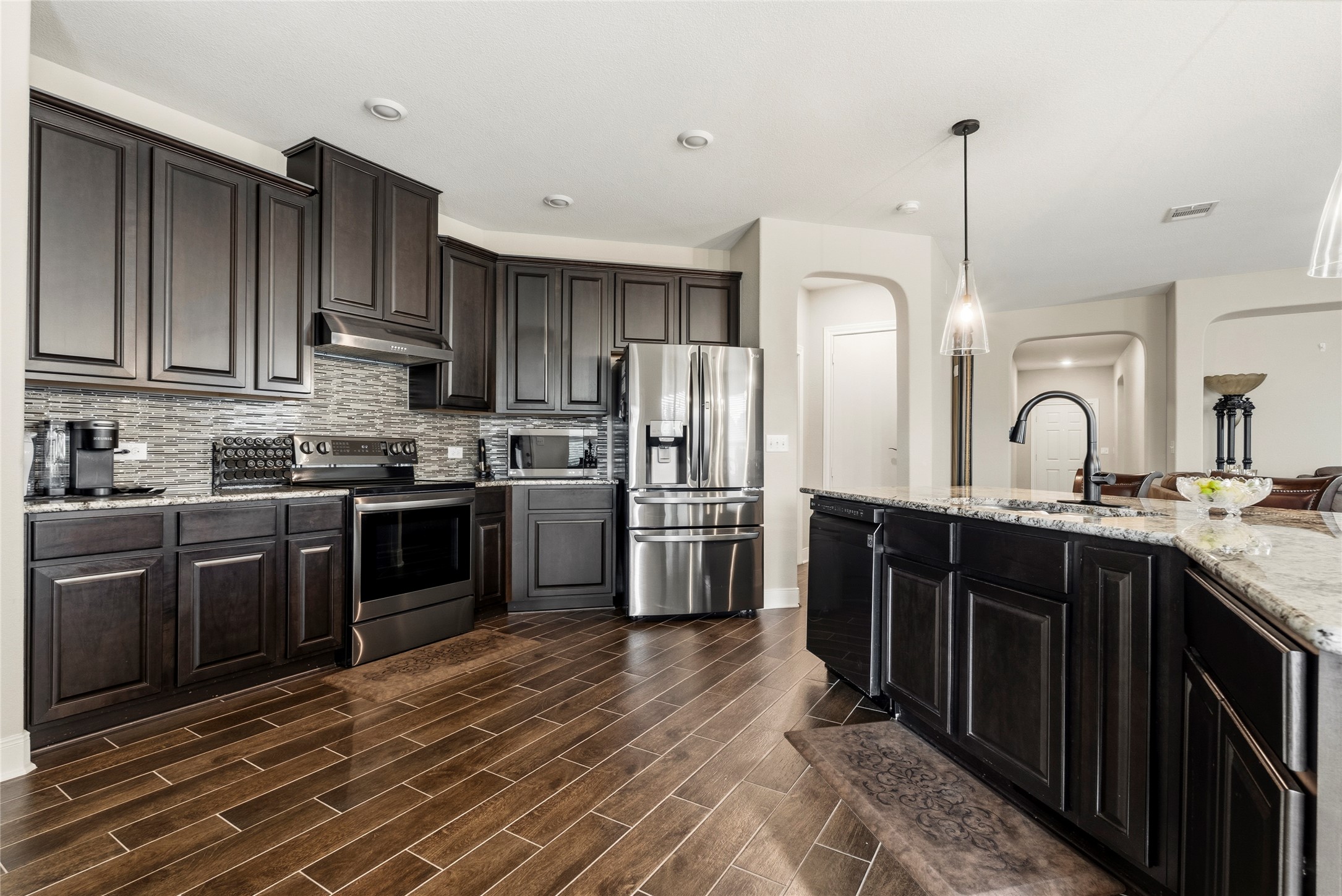 105 West Point Way Elgin, TX 78621 - Photo 3 of 27 Expansive kitchen featuring dark wood cabinetry, granite countertops, stainless steel appliances, a mosaic tile backsplash, and wood-finish flooring