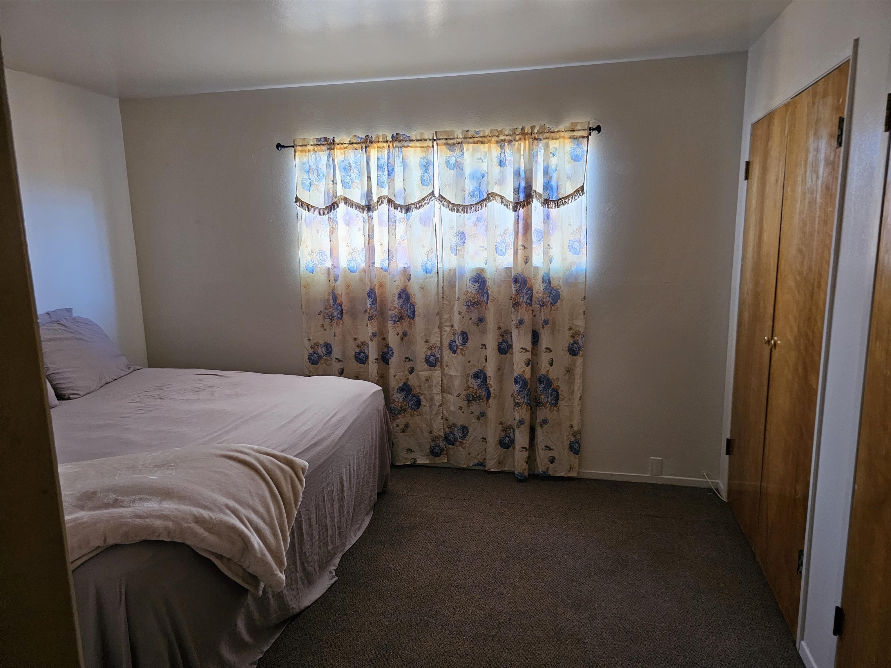 363 Short Street Bishop, CA 93514 - Photo 16 of 17 Carpeted room featuring a window with patterned curtains, light-colored walls, and two wood-finish bifold closet doors