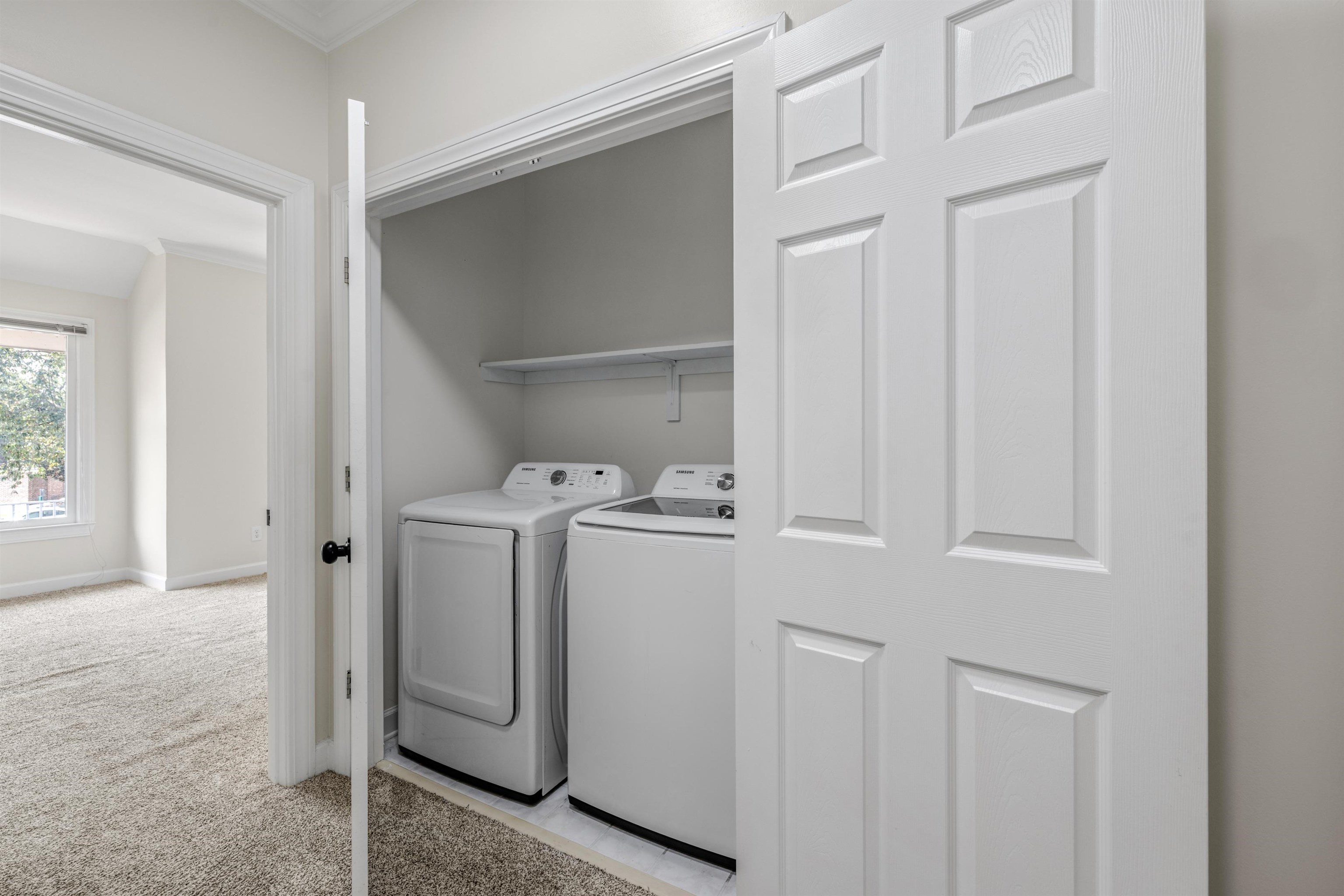 921 Harbor View Drive Memphis, TN 38103 - Photo 31 of 33 Dedicated laundry closet featuring a built-in shelf, white paneled bifold doors, and an adjacent carpeted room with a window
