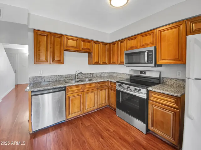 a kitchen with stainless steel appliances granite countertop wooden cabinets a stove top oven a sink and dishwasher with wooden floor