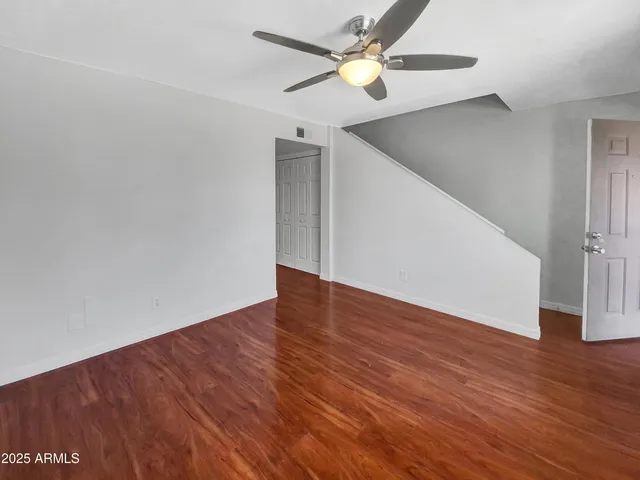 a view of an empty room with wooden floor and a ceiling fan
