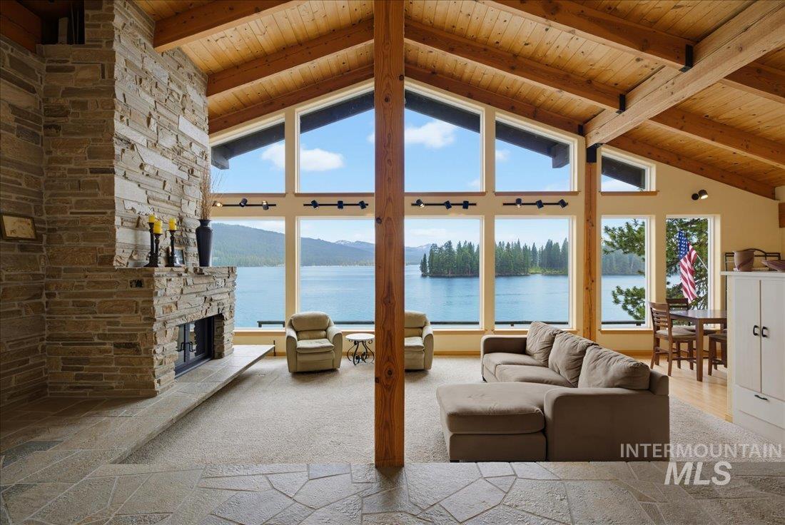 3800 Warren Wagon Road McCall, ID 83638 - Photo 10 of 50 Spacious living area featuring a vaulted wood-finish ceiling with exposed beams, a large stone fireplace, and expansive windows showcasing a prominent lake and island scenery