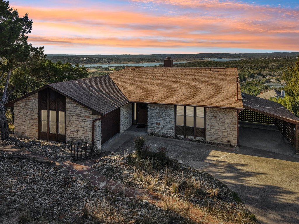 21009 Fawn Ridge Drive Lago Vista, TX 78645 - Photo 3 of 40 View of front of home with stone siding, roof with shingles, a chimney, concrete driveway, and a garage