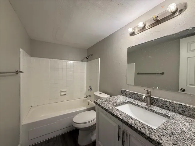a bathroom with a granite countertop sink a toilet a mirror and shower