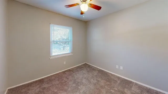 an empty room with chandelier fan and windows