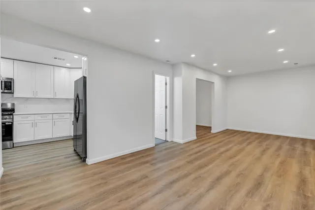 a view of an empty room with wooden floor and a kitchen