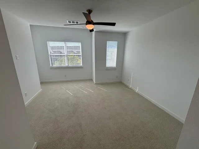 an empty room with a ceiling fan and a carpet