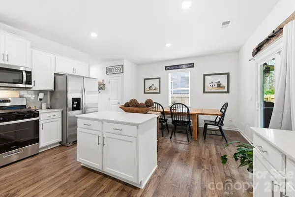 a open kitchen with stainless steel appliances granite countertop a dining table chairs stove refrigerator and cabinets