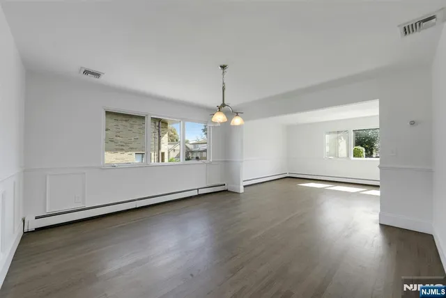 an empty room with wooden floor chandelier and windows